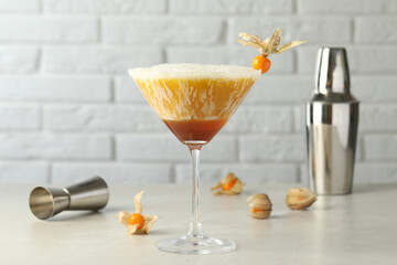 Delicious cocktail decorated with physalis fruit on light table near white brick wall