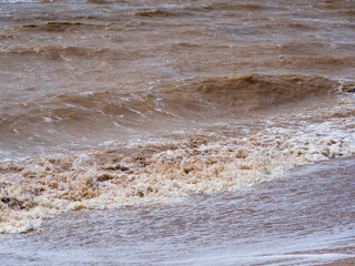 Muddy sea water from strong wind waves. Muddy brown waves roll onto the shore. Sea water with a suspension of clay from the erosion of the coastline