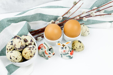 A bouquet of fluffy willow branches, Easter eggs and figures of hares on a light background. Happy Easter, Palm Sunday. Easter composition in the style of minimalism. Easter card.