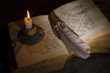 An open old book with a biblical text in Church Slavonic. A candle burns next to a book.