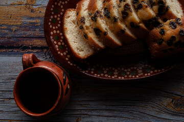 Dark food photography, black coffee in a Mexican clay jar with sweet bread and raisins slices, on an old rustic wooden table. Lay flat or top view of Dark Food Photography.