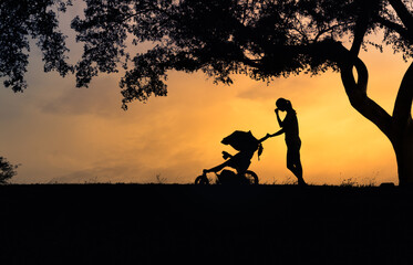 Silhouette of tired sad mother pushing stroller in the park. Parenting, post pardon depression, divorce  problems concept.  - obrazy, fototapety, plakaty