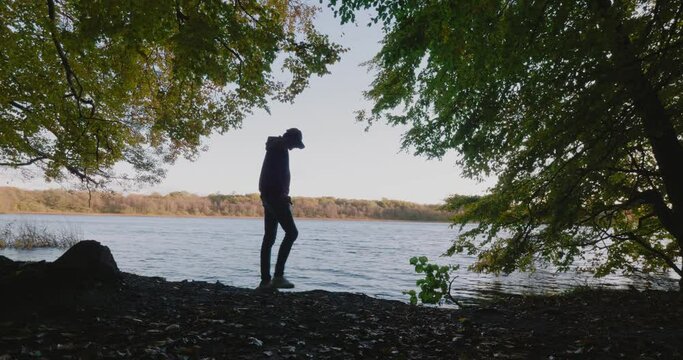 Tall Guy With Cap Searches For Rocks and Stuff in the Gyllebo Lake , Sweden Sk&aring;ne &Ouml;sterlen - Static Wide Shot Silhouette