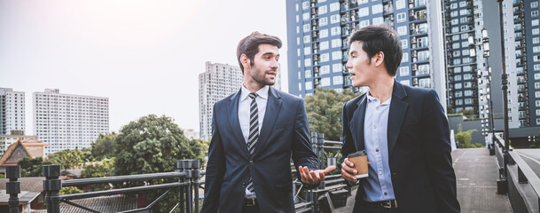 Asia businessman walking and talking to Caucasian businessman colleague while leaving office building after work, image panorama for cover design.