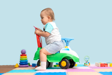 Toddler 15-20 months sitting on a children's toy car backwards in the playroom.