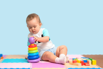 A kid of 15-23 months is sitting and assembling a pyramid toy, putting colorful rings on the plastic base of the tower.