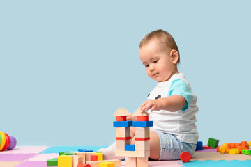 Toddler 12-17 months old builds a tower of wooden cubes sitting on the floor in the playroom. Copy space