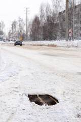 A metal storm sewer grate on a road covered with snow. Selective focus, vertical photo