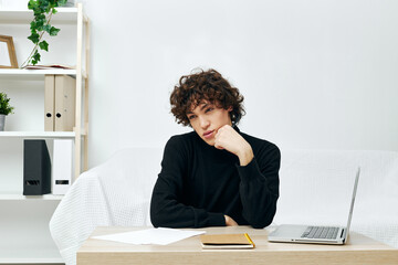 curly guy sitting on the couch at the table in front of a laptop communication