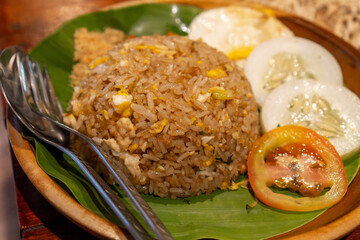 Nasi Goreng Cokelat. Fried rice mixed with egg, cucumber and sliced ​​tomatoes. served on a wooden plate with banana leaf.