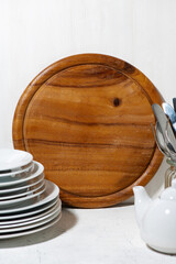 round wooden cutting board for writing down recipes and tableware on white table, vertical closeup