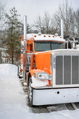 Orange classic big rig semi truck tractor with chrome parts standing on the winter truck stop...