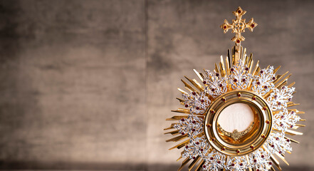 Catholic religion concept. Catholic symbols composition. The Cross, monstrance,  Holy Bible and golden chalice on wooden altar and gray background. 