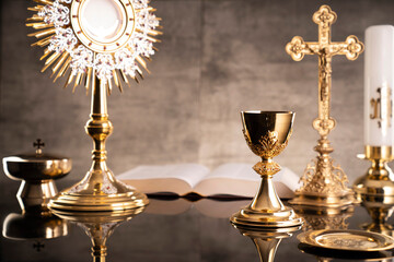 Catholic religion concept. Catholic symbols composition. The Cross, monstrance,  Holy Bible and golden chalice on wooden altar and gray background. 
