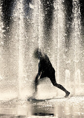 Silhouette of a kid dancing in the jets of cool fountain water on a hot summer day