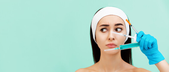 Banner of cosmetology. Portrait of a beautiful incredulous young woman holding syringes for...
