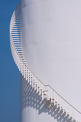 Naklejka premium Curve line of spiral staircase on white oil storage fuel tank with blue clear sky in vertical frame