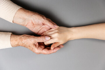 Fototapeta premium Grandmother is holding her granddaughter's hand. Hands close-up. Flat lay. Gray background. The concept of caring for pensioners