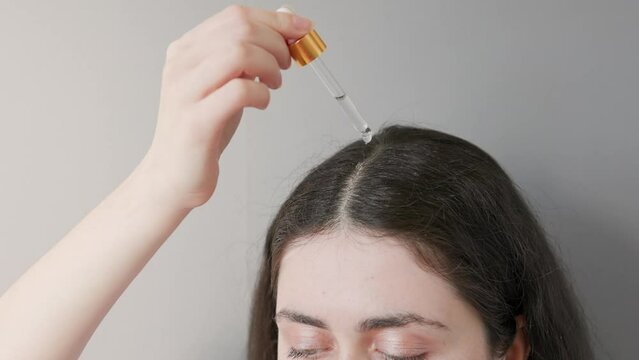 Portrait of a young Caucasian woman dripping cosmetic oil on a hair parting. Gray background. The concept of hair care.