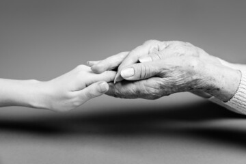 An elderly woman holds her daughter's hand in her palms. Close-up. Monochrome. The concept of...