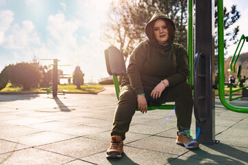 Self-confident overweight woman in a tracksuit posing at exercise equipment. Concept of fitness and...