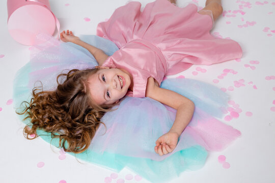 beautiful little girl in a chic pink dress lies on the floor strewn with confetti. top view. fashion and style. child celebrates his birthday. photo in the studio. space for text. High quality photo