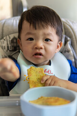 Adorable joyful and Happy 1 years old Chinese baby boy having food while sit on baby chair