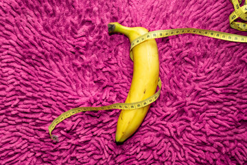 A banana and a yellow measuring tape surround it. Magenta color as background. Men's health concept.