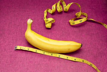 A banana and yellow measuring tape in magenta color as a background. Men's health concept.