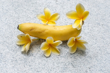 Fototapeta na wymiar Close up of a banana and yellow frangipani flowers in grey background. Erection and sex drive concept. Nutrition healthy diet.