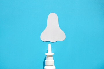 Paper silhouette of a nose and a can of spray on a blue background. Concept against allergic nasal...