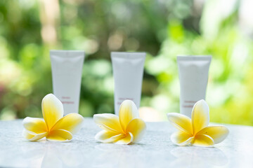 Three yellow frangipani flowers.  Three small bottles as a bokeh background.