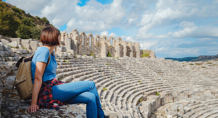 walk in Antalya Turkey on warm October afternoon. Pretty tourist woman with backpack at ruins of...