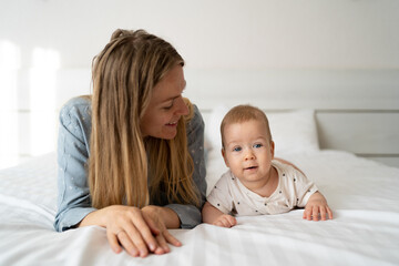 Portrait of a mother with a four month old baby in the bedroom. Young happy mum lies next to her adorable baby son, a cute blond boy playing