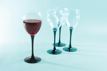 A glass of red wine and three empty glasses on a bluish background. 