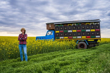 Proud female beekeeper is standing in front of her truck with beehives.