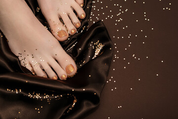 Female feet with golden nail design. Glitter gold nail polish pedicure with golden stars on brown background. Female feet with perfect golden pedicure