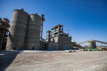 Modern cement plant in desert. Cement silos (tower), mixer silo, industrial building, asphalt road...