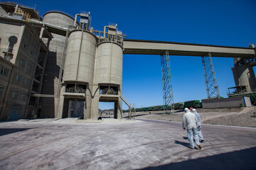 Modern cement plant in desert. Two workers in protective overalls or work wear and cement silo on...
