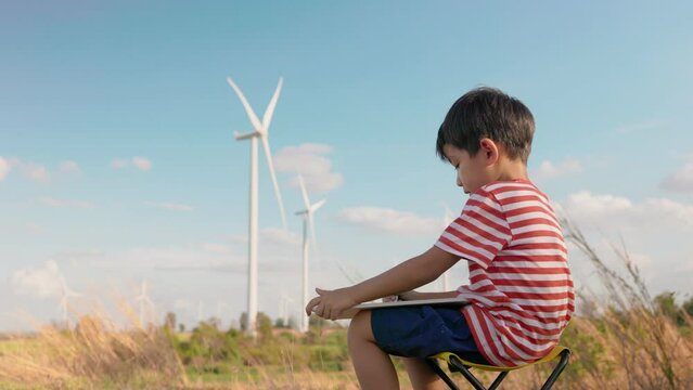Asian boy child draws pictures and take note on clean energy innovation in windmill farm field.