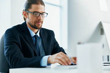 a man in a suit with glasses typing at his desk