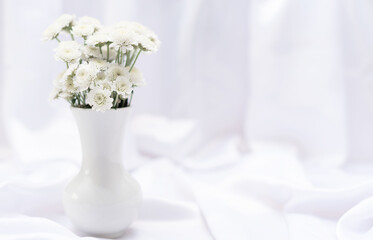 White flowers in white vase on white background with copy space and selective focus. Greeting or invitation card