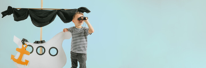 Little child boy playing with cardboard ship on blue wall background - obrazy, fototapety, plakaty