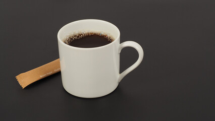 Hot coffee in white cup and brown sugar sachet isolated on black background.