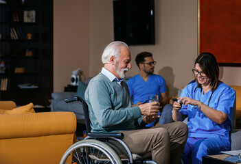 Naklejka premium Nurse helps an senior man in a wheelchair to take medication at nursing home.