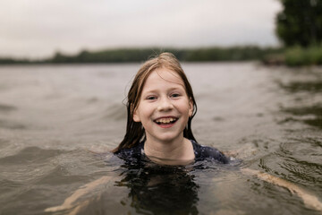 Happy girl swimming in lake at sunset