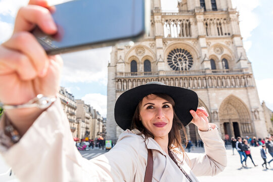 Young woman taking selfie on smart phone with Notre Dame Cathedral