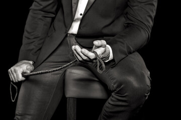 Rich man sitting on bar stool and holding whip, black and white, bdsm