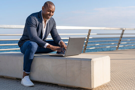 Smiling businessman using laptop sitting on bench at promenade