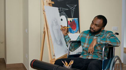African american man with disability using pencil to draw on canvas, learning new artistic skills...